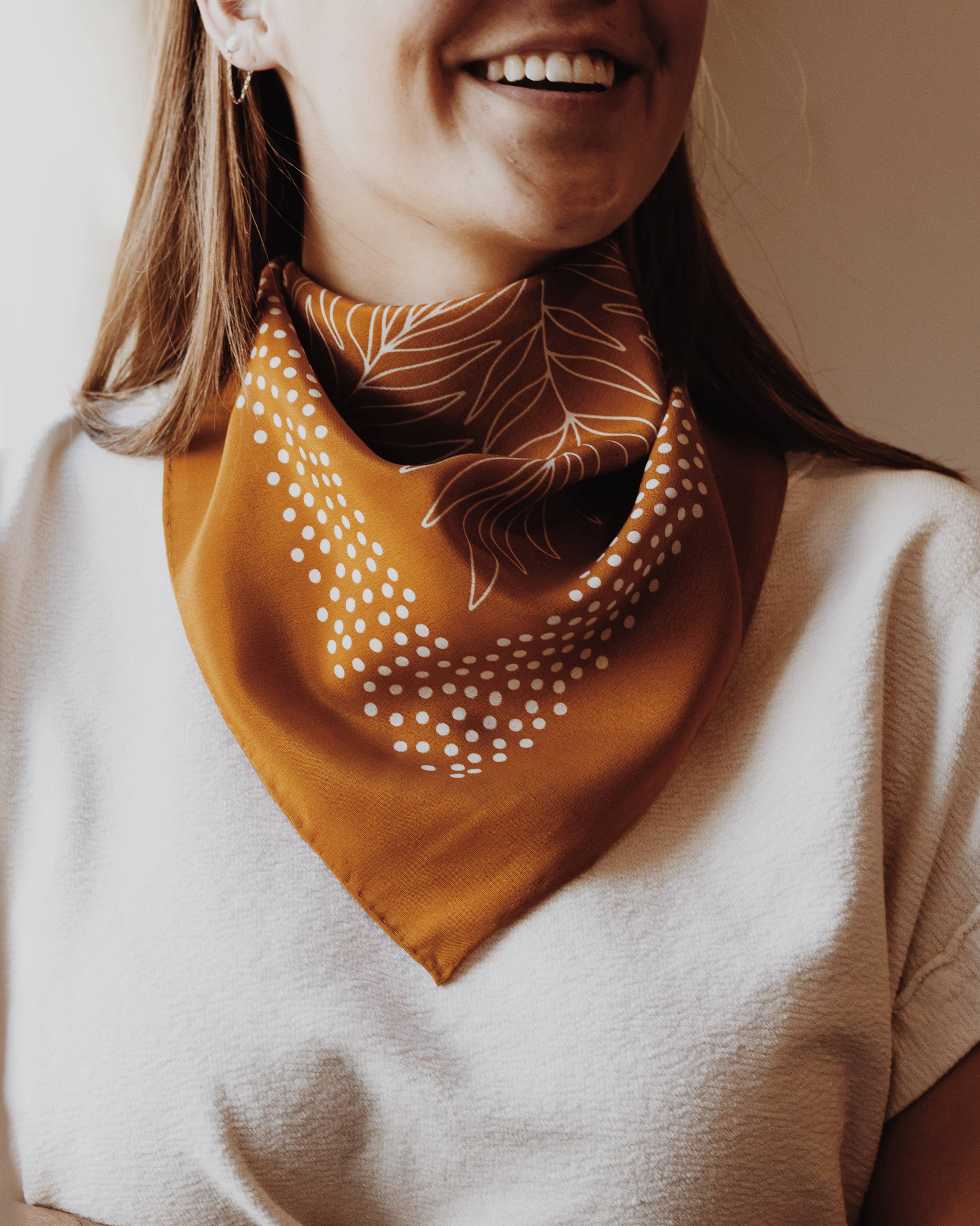 Person wearing a mustard yellow scarf with leaf pattern on a neutral background